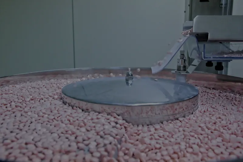 Bir makinenin dönen yüzeyinde toplanan ve oluktan dökülen küçük pembe tabletler