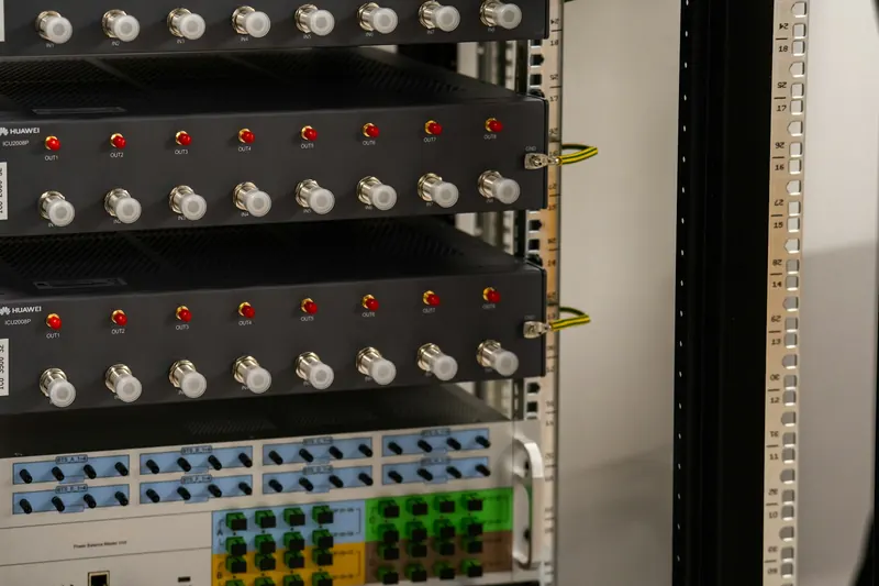 Bir sunucu kabininde üst üste dizilmiş ağ ve telekom ekipmanı; ön panellerde konnektörler ve kırmızı gösterge ışıkları