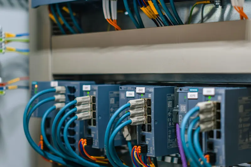 Endüstriyel bir kontrol panosunda mavi haberleşme kablolarıyla bağlanmış elektronik modüller