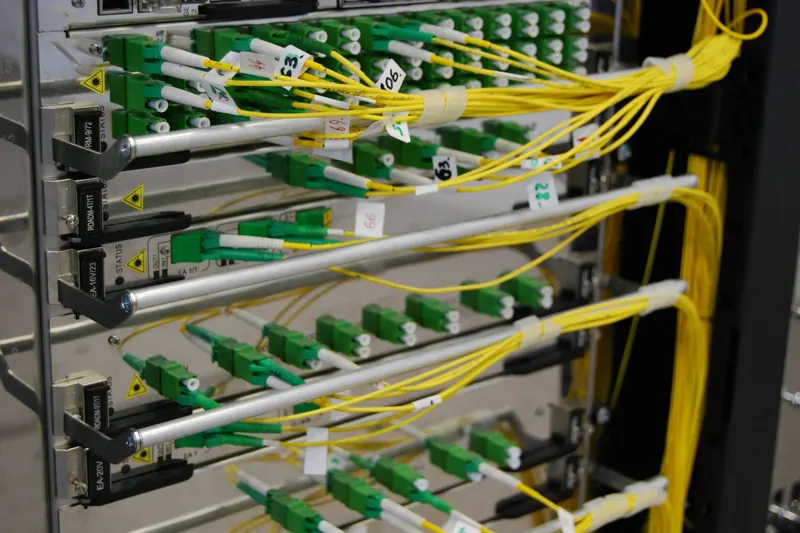 Optik ağ cihazının kartlarına bağlı sarı fiber optik patch kablolar ve yeşil konnektörler