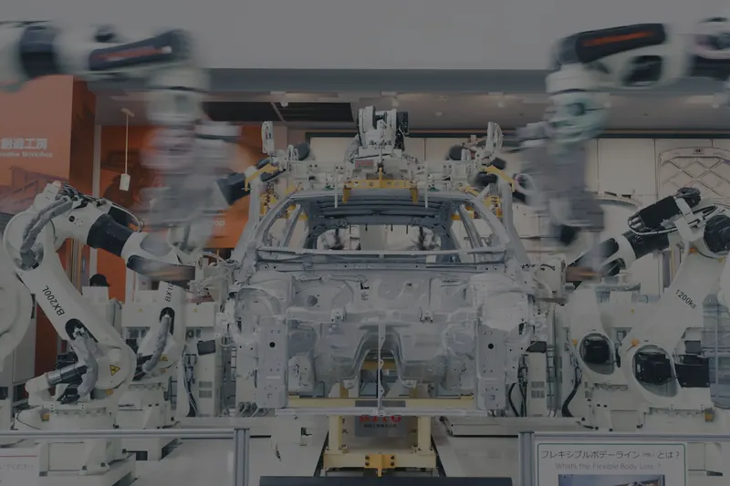 Bir otomobil gövdesinin çevresinde konumlanmış beyaz robot kollardan oluşan, sergilenen bir gövde kaynak hattı