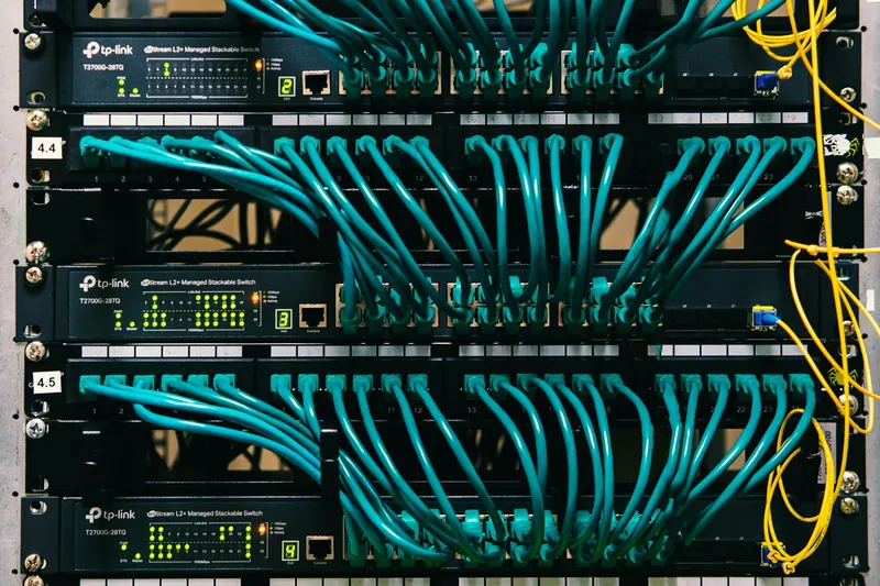 Rack kabindeki ağ anahtarlarına bağlı turkuaz patch kablolar ve yanlardan geçen sarı fiber kablolar