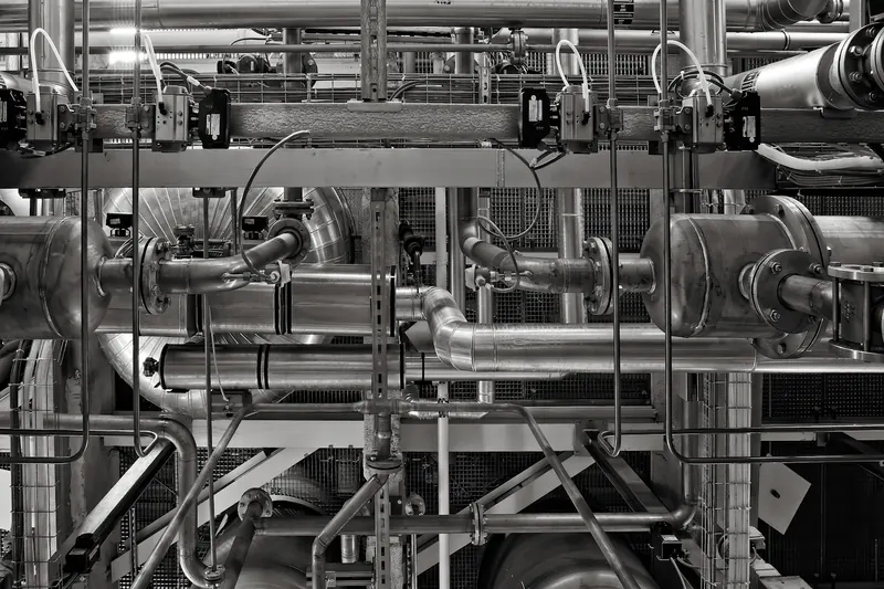 Bir sanayi tesisinde iç içe geçmiş metal borular, vanalar ve taşıyıcı çelik konstrüksiyon; siyah-beyaz