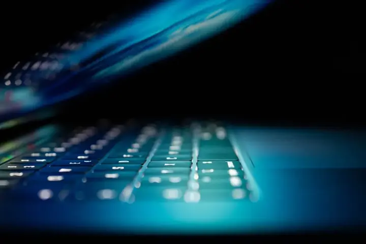 Low-angle close-up of a laptop keyboard glowing in blue light – IT and technology consulting